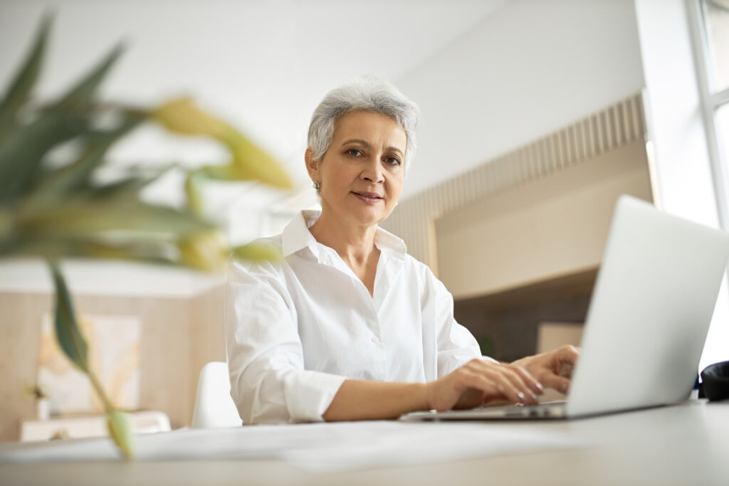 Indoor shot of stylish experienced female marketing expert sitting at desk in front of open generic portable computer, working to increase sales. People, technology, job and occupation concept